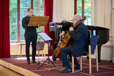 2026_Kurkonzert_Krenz_Jay 9.jpg Klassisches Trio spielt Geige, Cello und Klavier auf einer Bühne vor großen Fenstern.