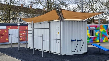 Trainieren auf dem Heeseplatz Weißer Fitness-Container mit Trainingsstangen und Sonnensegel auf Fallschutzmatten.