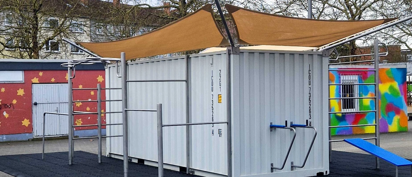 Trainieren auf dem Heeseplatz Weißer Fitness-Container mit Trainingsstangen und Sonnensegel auf Fallschutzmatten.