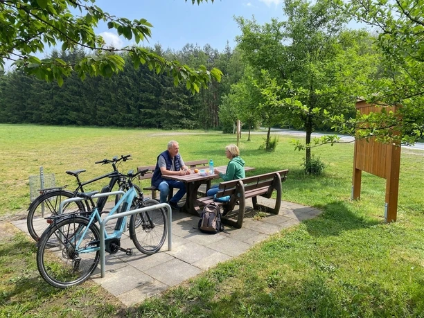 Radfahrer pausieren an Picknicktisch mit Fahrrädern am Rastplatz im Grünen bei Steinhagen