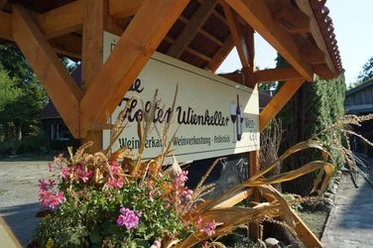 De Holter Wienkeller.jpg Überdachtes Holzschild des De Holter Wienkellers, verziert mit rosa Blumen und Maispflanzen.