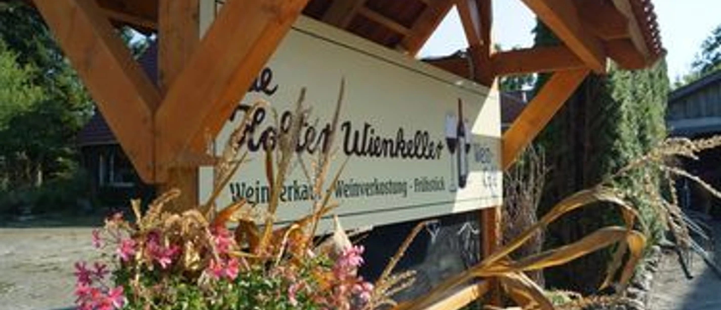 De Holter Wienkeller.jpg Überdachtes Holzschild des De Holter Wienkellers, verziert mit rosa Blumen und Maispflanzen.