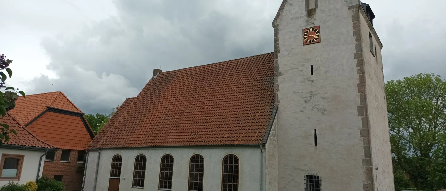 Kirche_Heerte_HD_16zu9.jpg Weiße Kirche St. Petri mit rotem Ziegeldach, dunklen Bogenfenstern und Turm mit Uhr.