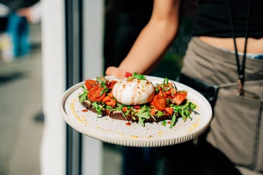 Das Café Ora bietet vegetarische und vegane Gerichte an Ein Teller mit einem belegten Brot mit Tomate und Burrata wird präsentiert