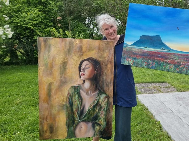 Frau hält zwei Gemälde: eines mit einer Frau und eines mit einer Landschaft.