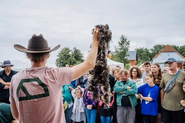 Nordwolle Werksfestival Person mit Hut präsentiert eine dunkle Wollfaser vor einer dicht versammelten Zuschauergruppe.
