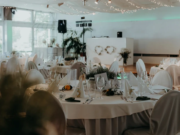 Tafelfreuden Festively set round tables with glasses, white chairs, and string lights in the hall