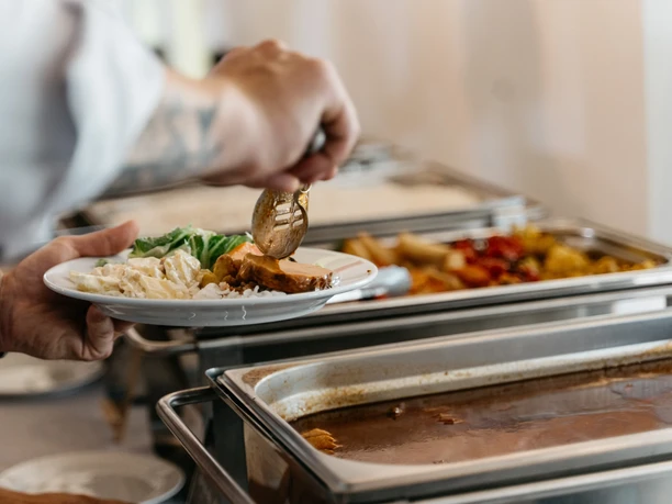 Tafelfreuden Catering-Ausgabe mit Teller, Salat, Reis, Fleisch und warmen Speisen in Edelstahlbehältern