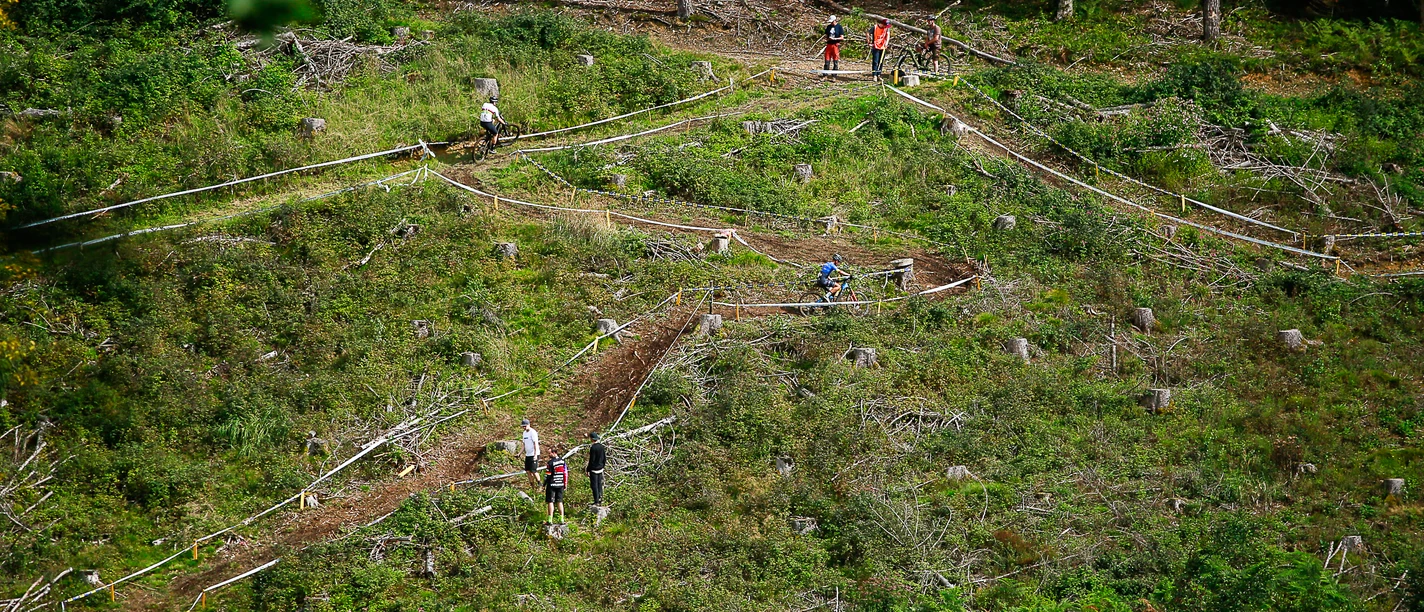 Bielsteiner Waldkurs Mountainbiker auf kurvigem Waldkurs zwischen Lichtungen und Beobachtern am Hang.