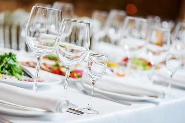 Gedeckter Tisch mit drei verschieden großen Weingläsern, Tellern, Servietten und Salate in der Tischmitte.