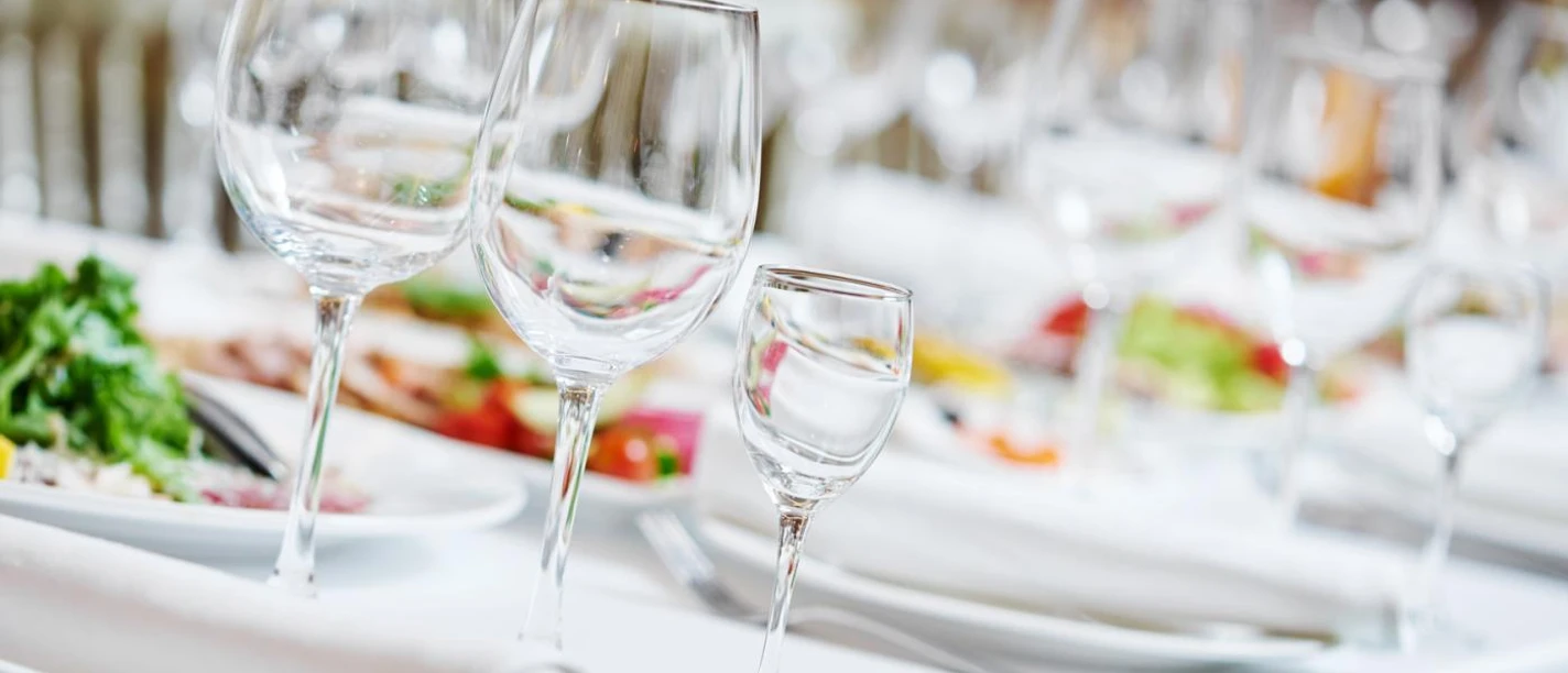 Gedeckter Tisch mit drei verschieden großen Weingläsern, Tellern, Servietten und Salate in der Tischmitte.