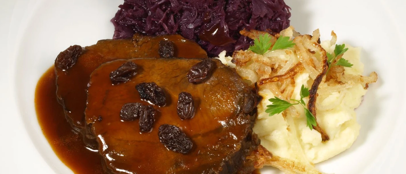 Aachener Brauhaus Degraa Auf einem Teller ist Sauerbraten mit Rosinen, Kartoffelpürree und Rotkohl angerichtet