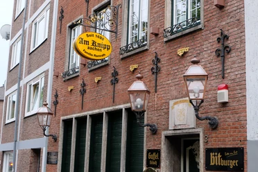 Außenansicht und Fassade des Restaurants "Am Knipp". Sie ist geschmückt mit alten Laternen und Verzierungen. Zwischen den Fenstern des Erdgeschosses und der ersten Etage hängt ein Schild an einer Halterung, auf dem der Name des Restaurants steht.
