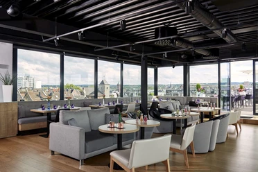 Raum mit Sofas, runden Tischen und Stühlen und Fensterfront mit Blick über Aachener Dächer.