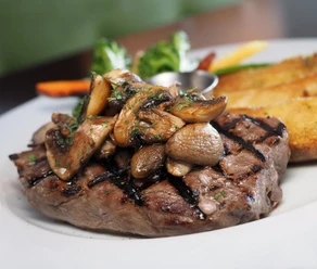 Steak, auf dem gebratene Champignons liegen, und Salat im Hintergrund.