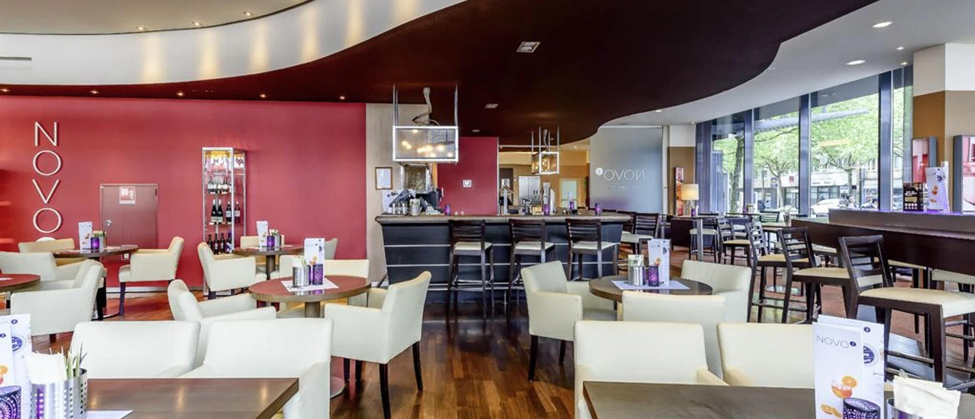 NOVO² - Novotel Aachen City Innenraum mit Sitzgruppen und einer Theke mit hohen Barstühlen.