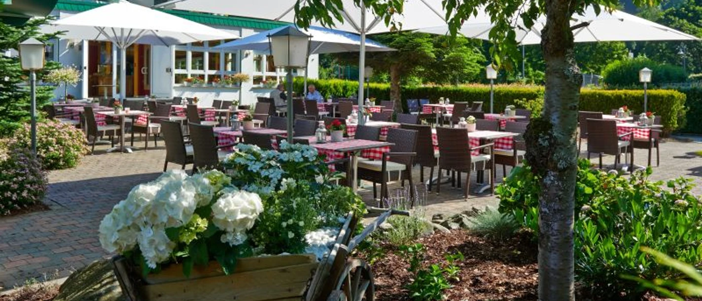 Außenbereich Restaurant Landhotel Kallbach Außenbereich mit einigen Sitzgruppen und Sonnenschirmen umgeben von Beeten und Hecken. Im Hintergrund steht ein Haus.