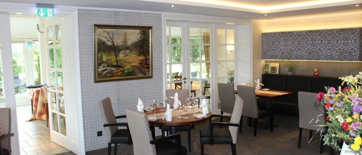 Innenansicht Landgasthof Gut Marienbildchen Innenraum mit mehreren Sitzgruppen, einem Gemälde von einer Naturlandschaft an der Wand und Teppichboden.