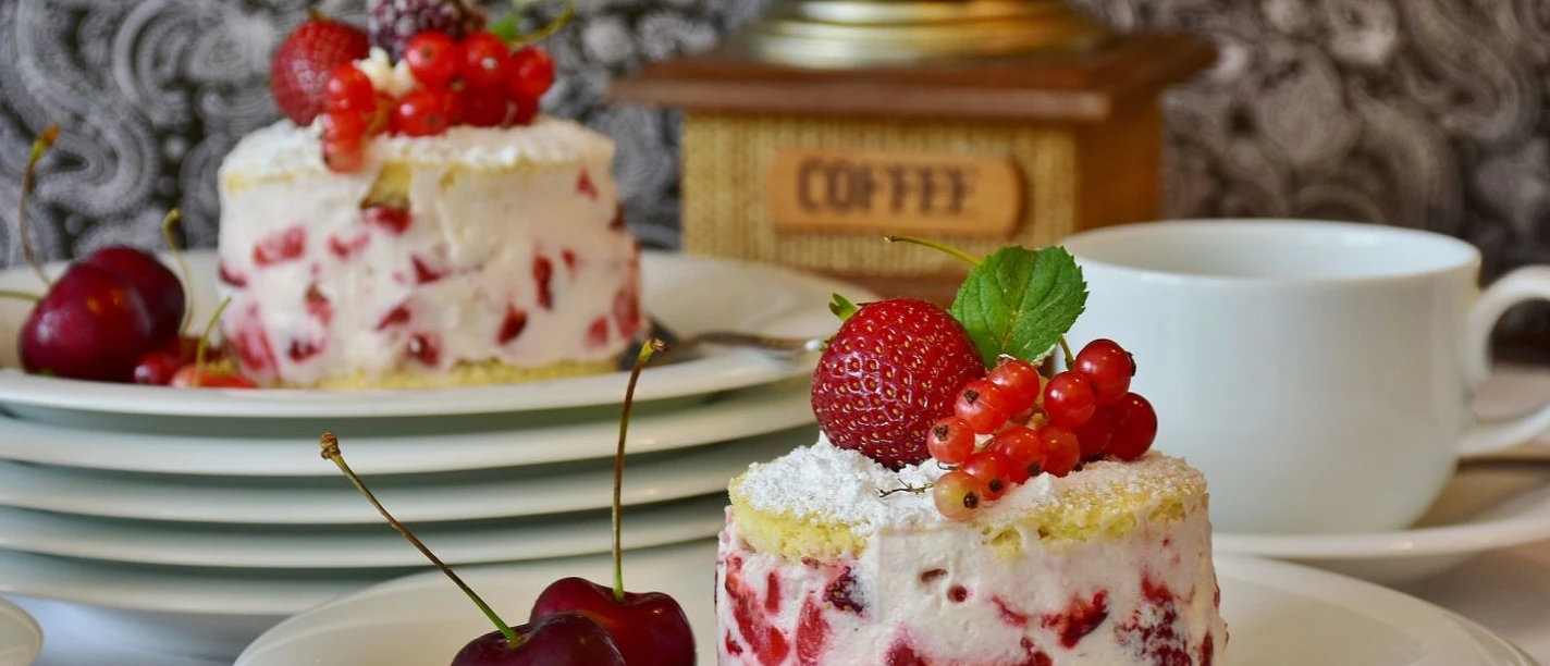 Café van den Daele Nahaufnahme von einem Teller, auf dem ein rundes Stück Kuchen mit Erdbeeren und Johannisbeeren steht. Im Hintergrund stehen gestapelte Teller, wobei auf dem oberen auch ein solches Kuchenstück liegt.