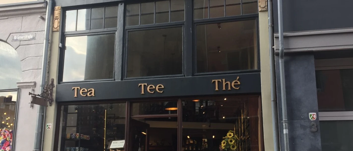 Dunkle Fassade mit der Aufschrift "Haus Eulenspiegel" und "Tea", "Tee" und "Thé" darunter. Hinter dem Schaufenster im Erdgeschoss ist Ware ausgestellt. Der Eingang befindet sich in der Mitte.