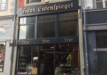 Der Teeladen - Haus Eulenspiegel Dunkle Fassade mit der Aufschrift "Haus Eulenspiegel" und "Tea", "Tee" und "Thé" darunter. Hinter dem Schaufenster im Erdgeschoss ist Ware ausgestellt. Der Eingang befindet sich in der Mitte.