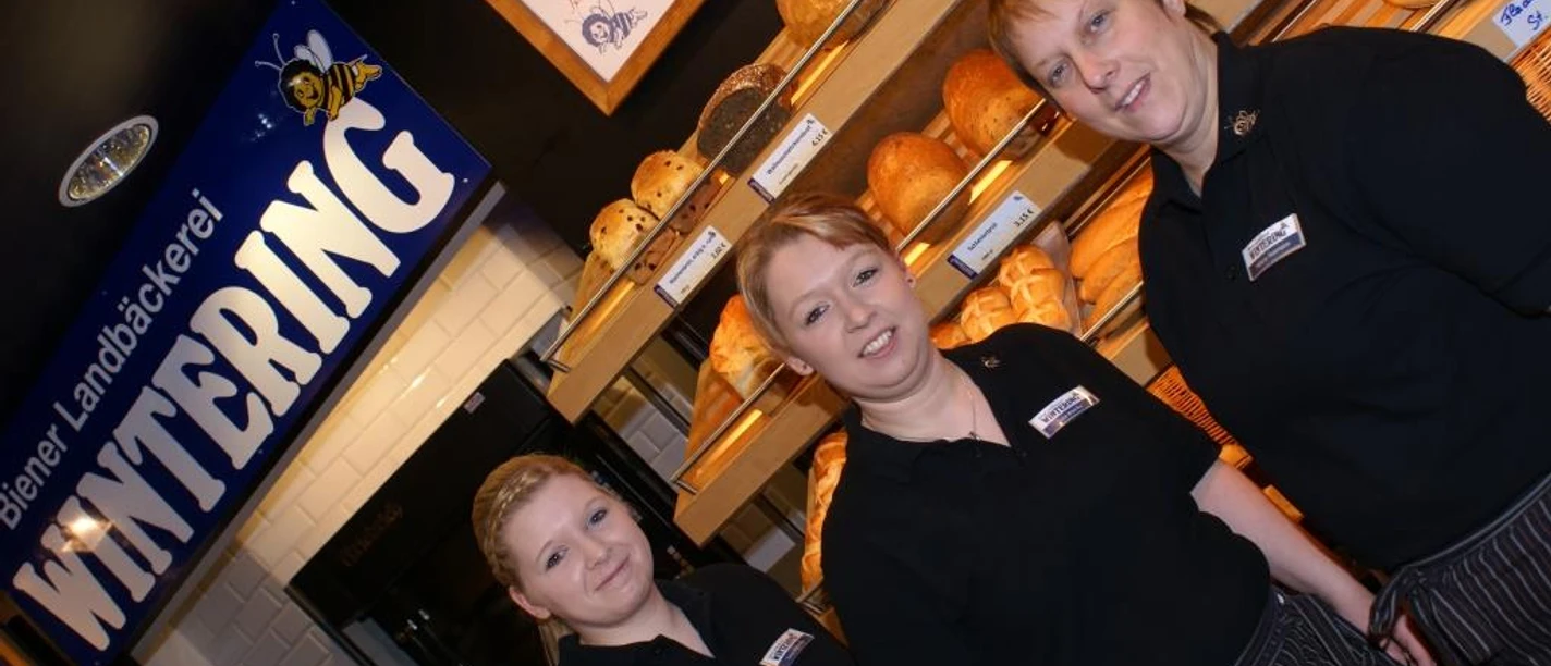 Team_Rhede_1_klein.jpg Drei Mitarbeitende der Biener Landbäckerei Wintering stehen vor Regalen mit frischem Brot.