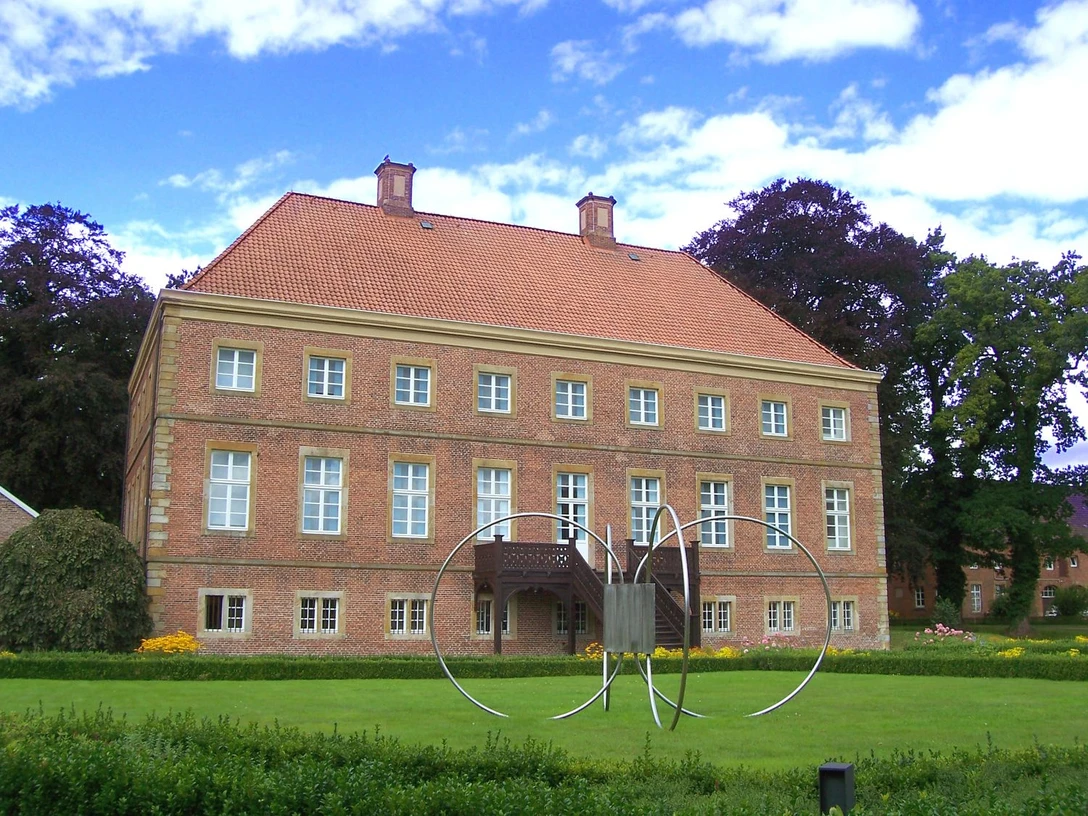 Emsland_-_Aschendorf_-_Gut_Altenkamp_-_Aussenansicht_vom_Park_auf_das_Herrenhaus.jpg Backsteinernes Herrenhaus Gut Altenkamp mit rotem Ziegeldach, gepflegtem Park und moderner Skulptur.