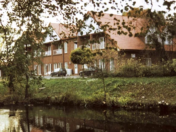 H_ZurEmsbruecke_Haus_Lathen.jpg Backsteingebäude mit rotem Dach am Flussufer, umgeben von Bäumen und herbstlicher Vegetation.