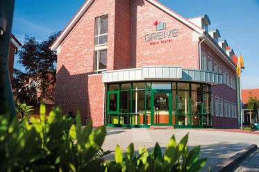 HotelGreive_Haren6_mini.jpg Backsteinbau mit grünem Eingang und Glasfront des barrierefreien Hotel Greive in Haren an einem sonnigen Tag