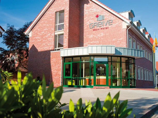 HotelGreive_Haren6_mini.jpg Backsteinbau mit grünem Eingang und Glasfront des barrierefreien Hotel Greive in Haren an einem sonnigen Tag