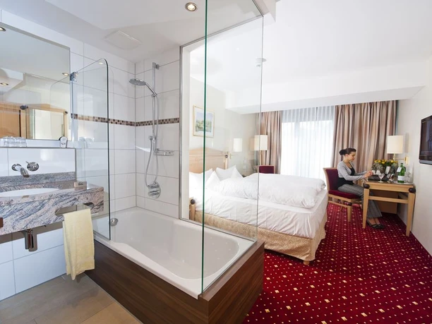 Hotel_Pöker_Doppelzimmer Modernes Doppelzimmer mit integriertem Bad, rotem Teppich, Schreibtisch und großer Fensterfront
