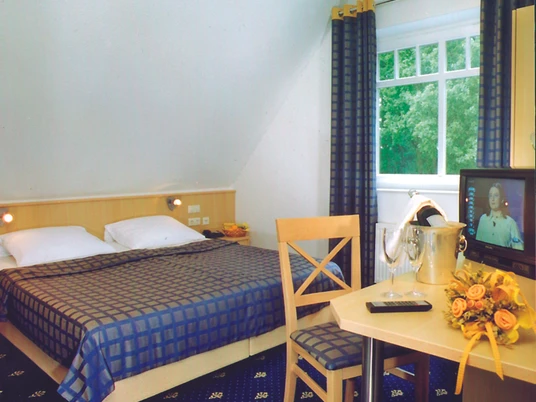 H_LathenerMarsch_Zimmer.jpg Doppelzimmer mit blau kariertem Bett, Schreibtisch mit Fernseher, Blumenstrauß und Ausblick ins Grüne.