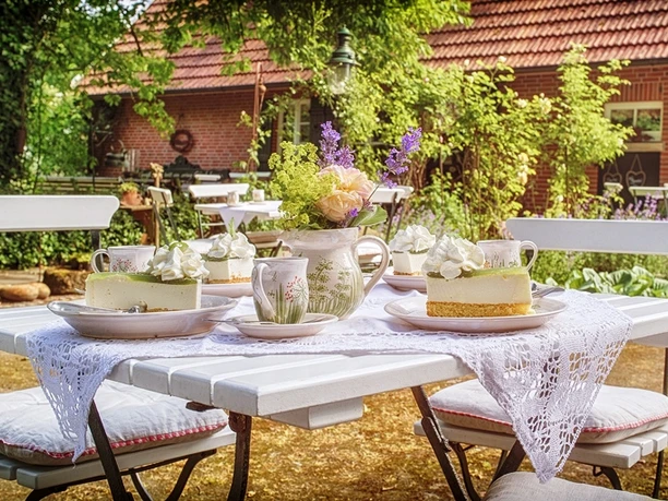 emsland-emsland-touristik-markus-kreihe-8 Weiß gedeckter Gartentisch mit Blumenstrauß, Kuchenstücken und Geschirr vor rotem Backsteinhaus