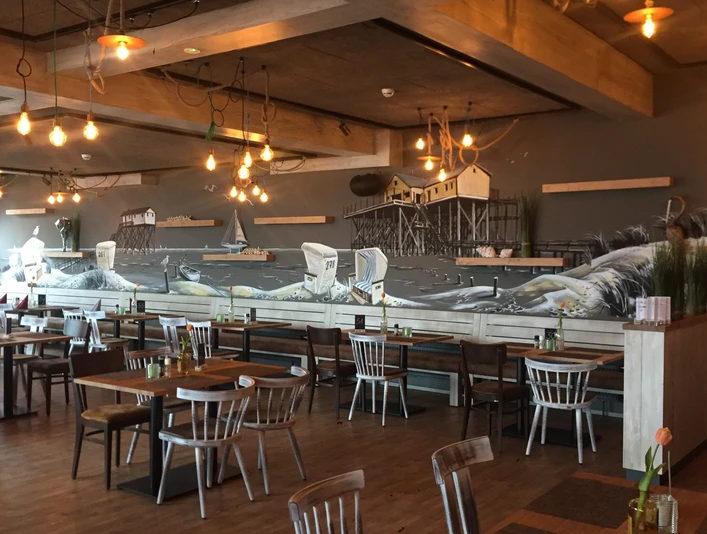 deichkrone-johanna-l-bbers-15 Holzverkleideter Gastraum mit maritimer Wandmalerei, Hängeleuchten und liebevoll gedeckten Tischen.