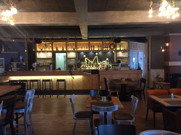 Holzverkleidete Bar mit beleuchteten Regalen, Tischen und Stühlen in warmem Lichtambiente
