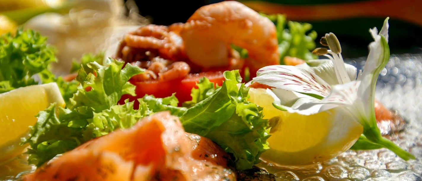 Nahaufnahme von einem Salat mit Lachs, Garnelen, einer Tomate und Zitronenspalten.
