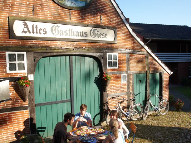 Altes Gasthaus Giese Vier Personen sitzen im Hof vor dem Backsteinhaus Altes Gasthaus Giese und essen gemeinsam.