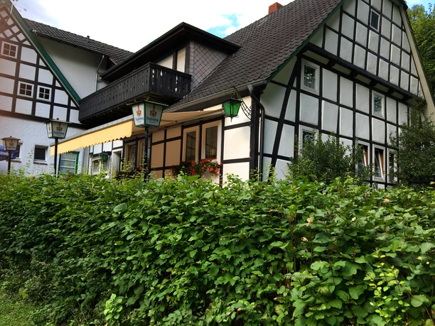 Café Sutthauser Mühle Backsteingebäude in Fachwerkoptik mit Laternen und üppigem Grün umgeben unter einem blauen Himmel.