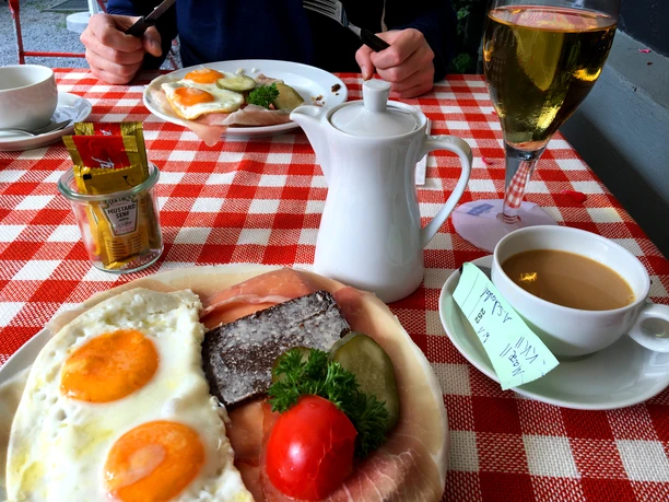 Ontbijtbord met gebakken ei, ham en groenten op een rood-wit geblokte tafel in Café Sutthauser Mühle.