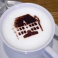 StadtGalerieCafé Kaffee mit aufgeschäumter Milch, verziert mit dem Kakaobild eines historischen Gebäudes.