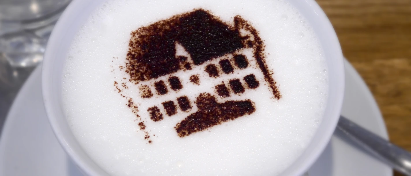 StadtGalerieCafé Kaffee mit aufgeschäumter Milch, verziert mit dem Kakaobild eines historischen Gebäudes.