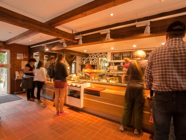 milchhalle-innen Besucher stehen am Tresen eines gemütlichen Cafés mit Backsteinwänden und hölzernen Deckenbalken.