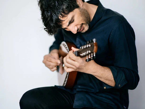 Avi Avital Musiker spielt konzentriert eine kleine Saitenlaute vor hellem Hintergrund.