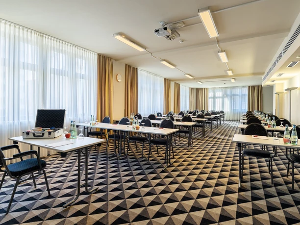 Bright meeting room with rows of tables, chairs, drinks and large window front light.