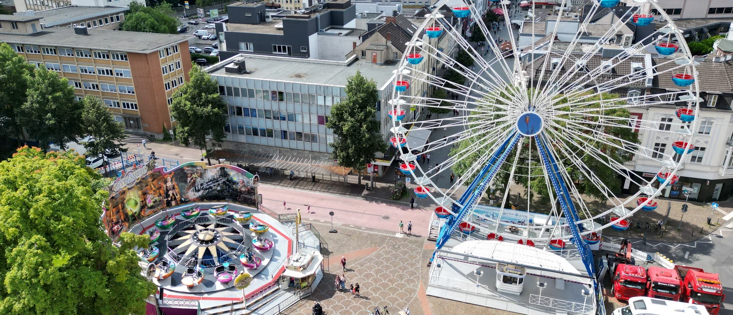 Pfingstkirmes Luftaufnahme einer Kirmes mit großem Riesenrad, Fahrgeschäften und umgebenden Stadtgebäuden