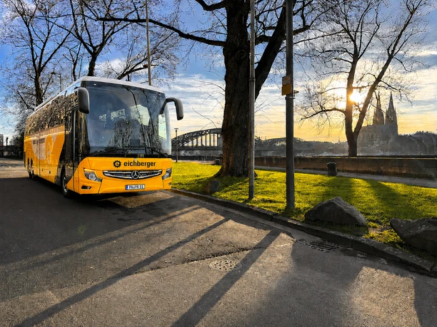 Bus vor Dom Gelber Reisebus am Rheinufer mit Brücke und Dom im warmen Abendlicht.