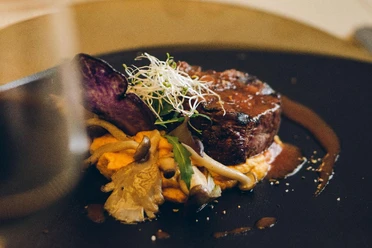 Steak in einer Soße auf einem Teller garniert mit Pilzen und Sprossen.