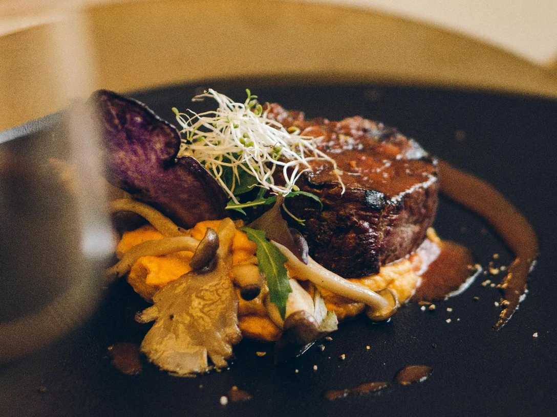 Steak in einer Soße auf einem Teller garniert mit Pilzen und Sprossen.