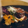Restaurant Luna Steak in einer Soße auf einem Teller garniert mit Pilzen und Sprossen.