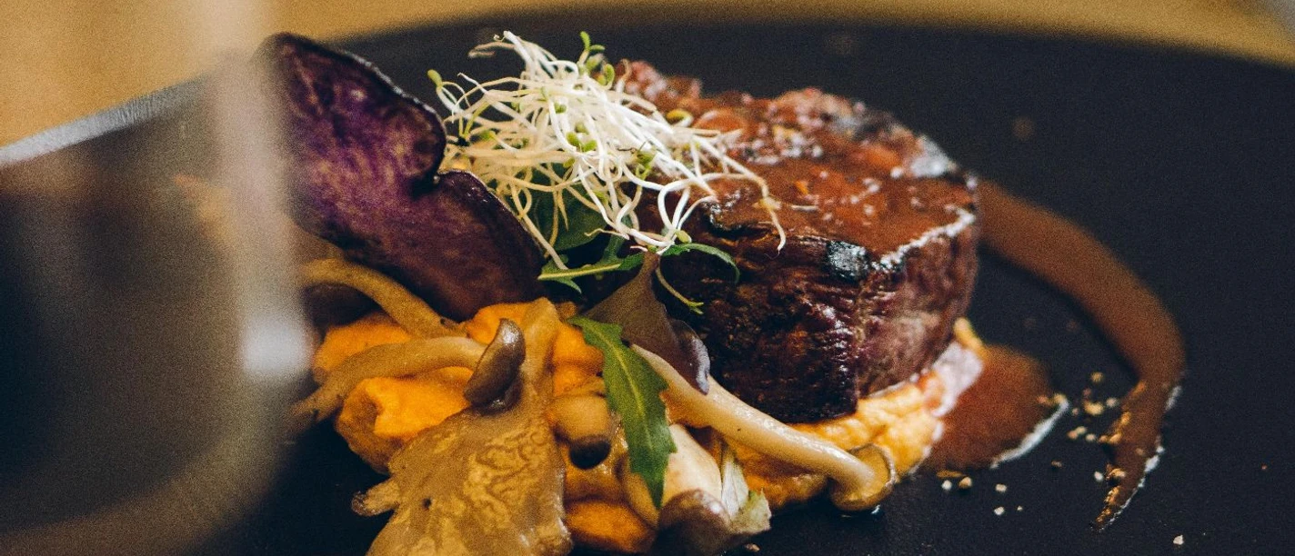 Restaurant Luna Steak in einer Soße auf einem Teller garniert mit Pilzen und Sprossen.